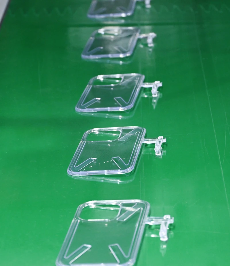 Freshly molded polycarbonate (PC) phone case base materials moving on the conveyor belt next to injection molding machines for immediate quality inspection.